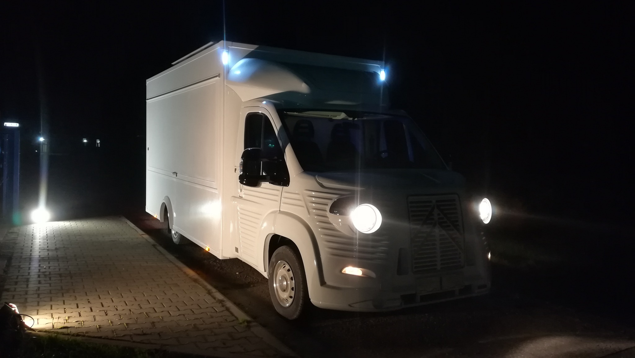 Biały samochód dostawczy Citroën HY z nadbudową typu kontener, sfotografowany nocą z włączonymi światłami przednimi i obrysowymi.