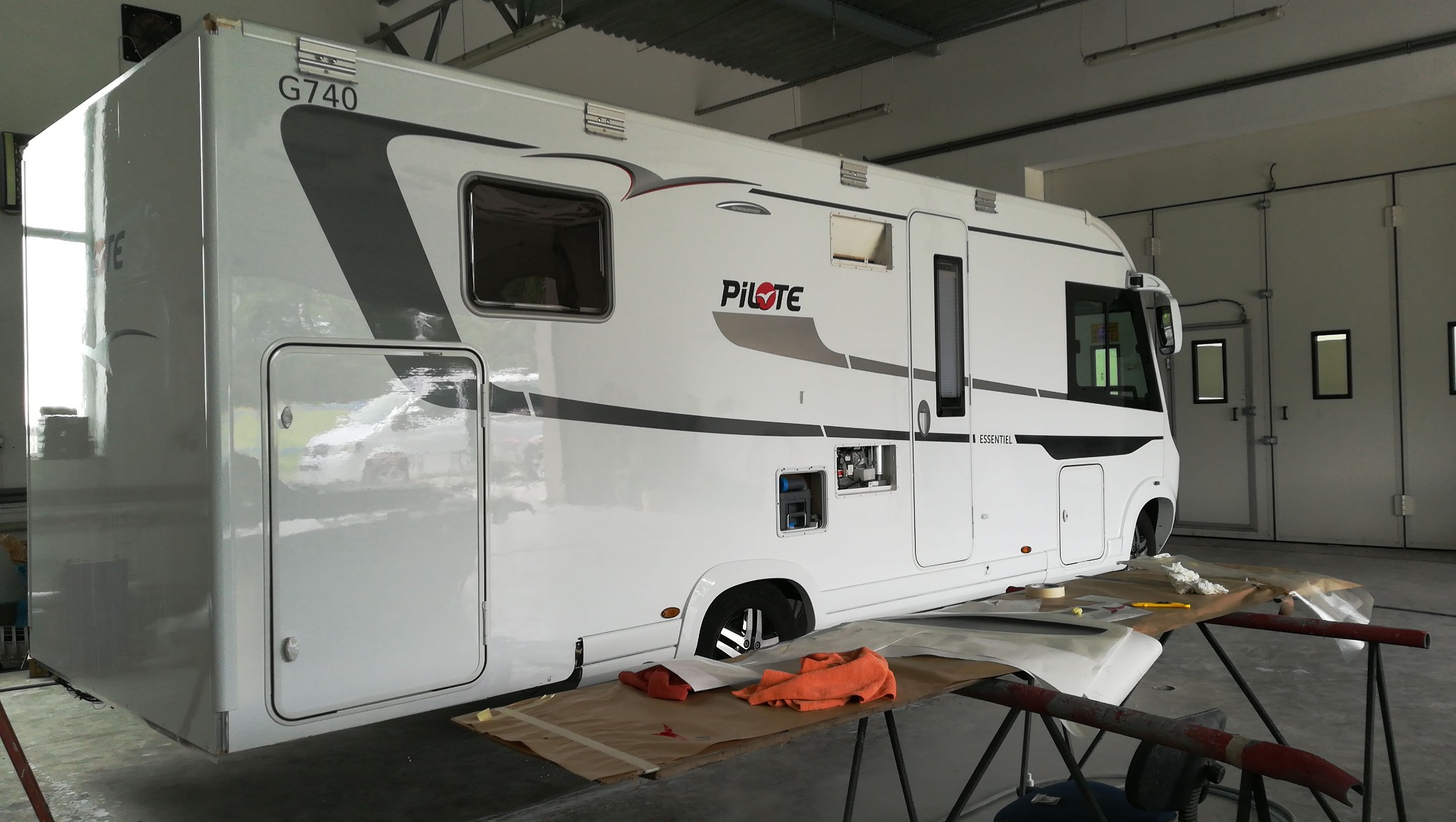 Biały kamper Pilote G740 w warsztacie, częściowo oklejony papierem maskującym, przygotowywany do prac lakierniczych.