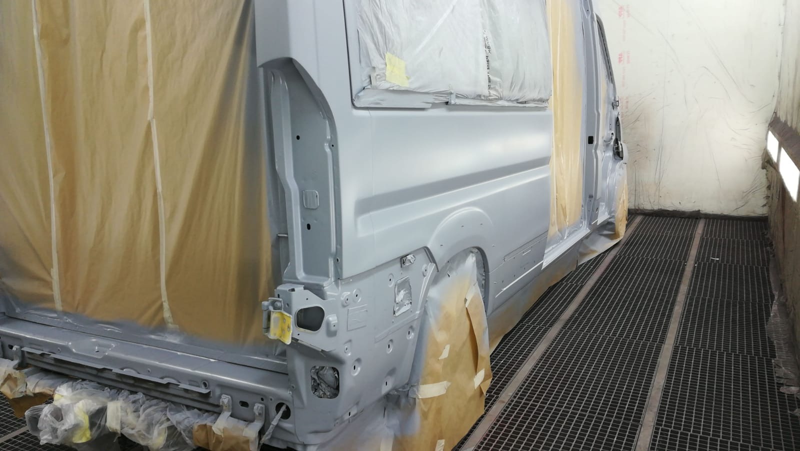 Przygotowany do lakierowania bus w kabinie lakierniczej, z widocznymi elementami maskującymi i świeżo nałożonym podkładem.