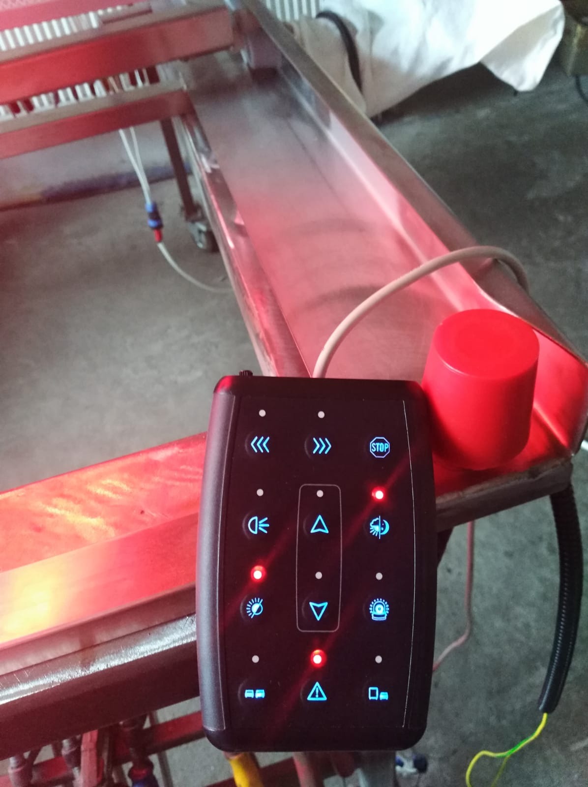 Panel sterowania z podświetlanymi przyciskami, umieszczony obok metalowej konstrukcji oświetlonej na czerwono.