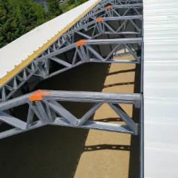 Konstrukcja stalowa poddasza z widoczną izolacją i blachą trapezową, z elementami mocującymi w kolorze pomarańczowym.