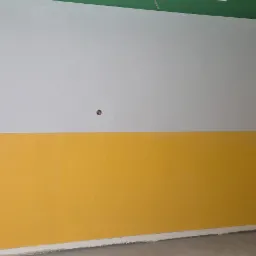 Ściana po malowaniu: g&oacute;ra biała, d&oacute;ł ż&oacute;łty, zielony sufit. Widoczny fragment podłogi i narożnik. Realizacja w pomieszczeniu oświetlonym naturalnym światłem.