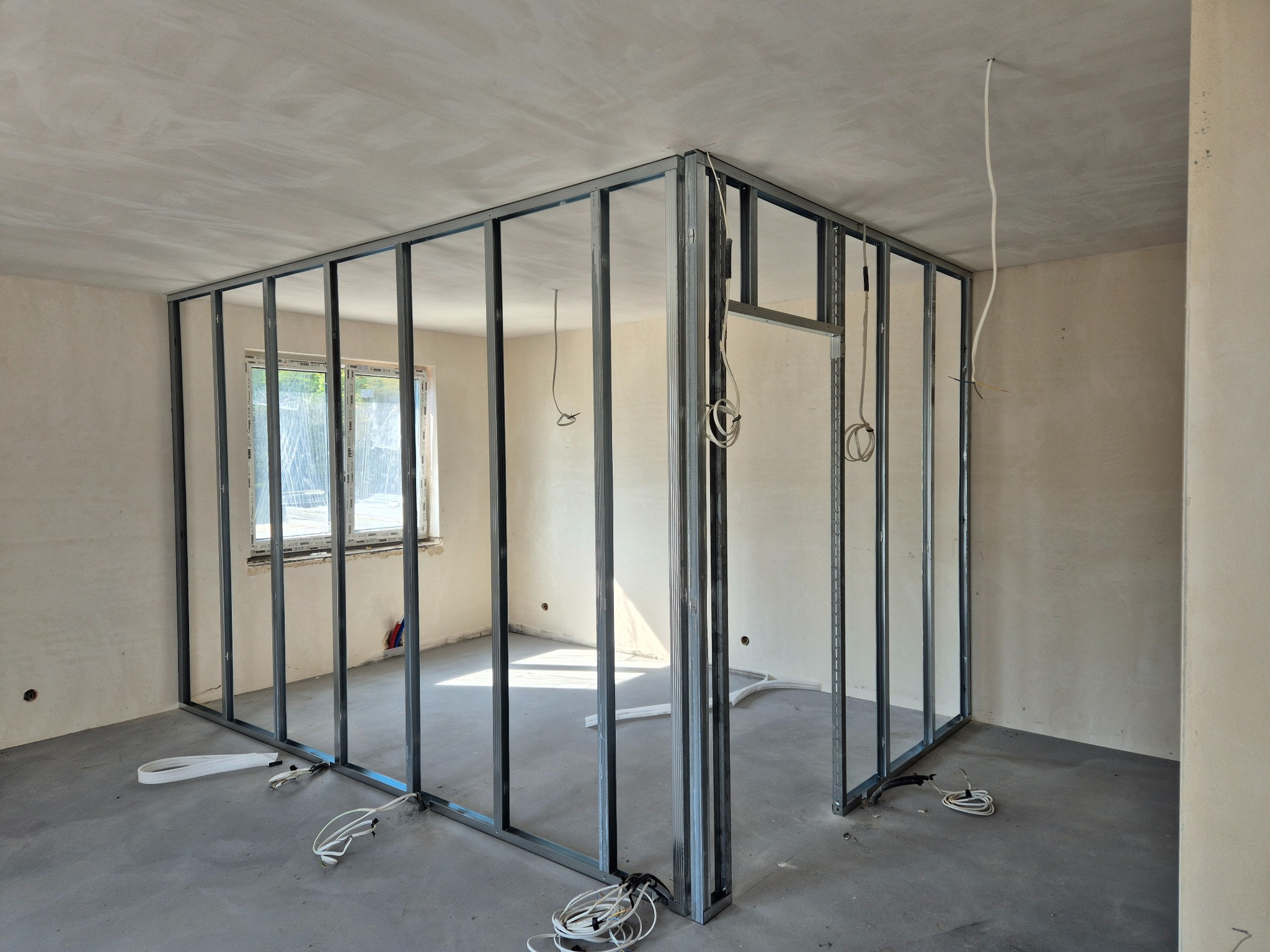 Wnętrze w trakcie montażu ścian działowych z metalowych profili, widoczne przewody elektryczne. Surowe wykończenie ścian i podłogi. Kąt ujęcia z narożnika pomieszczenia.