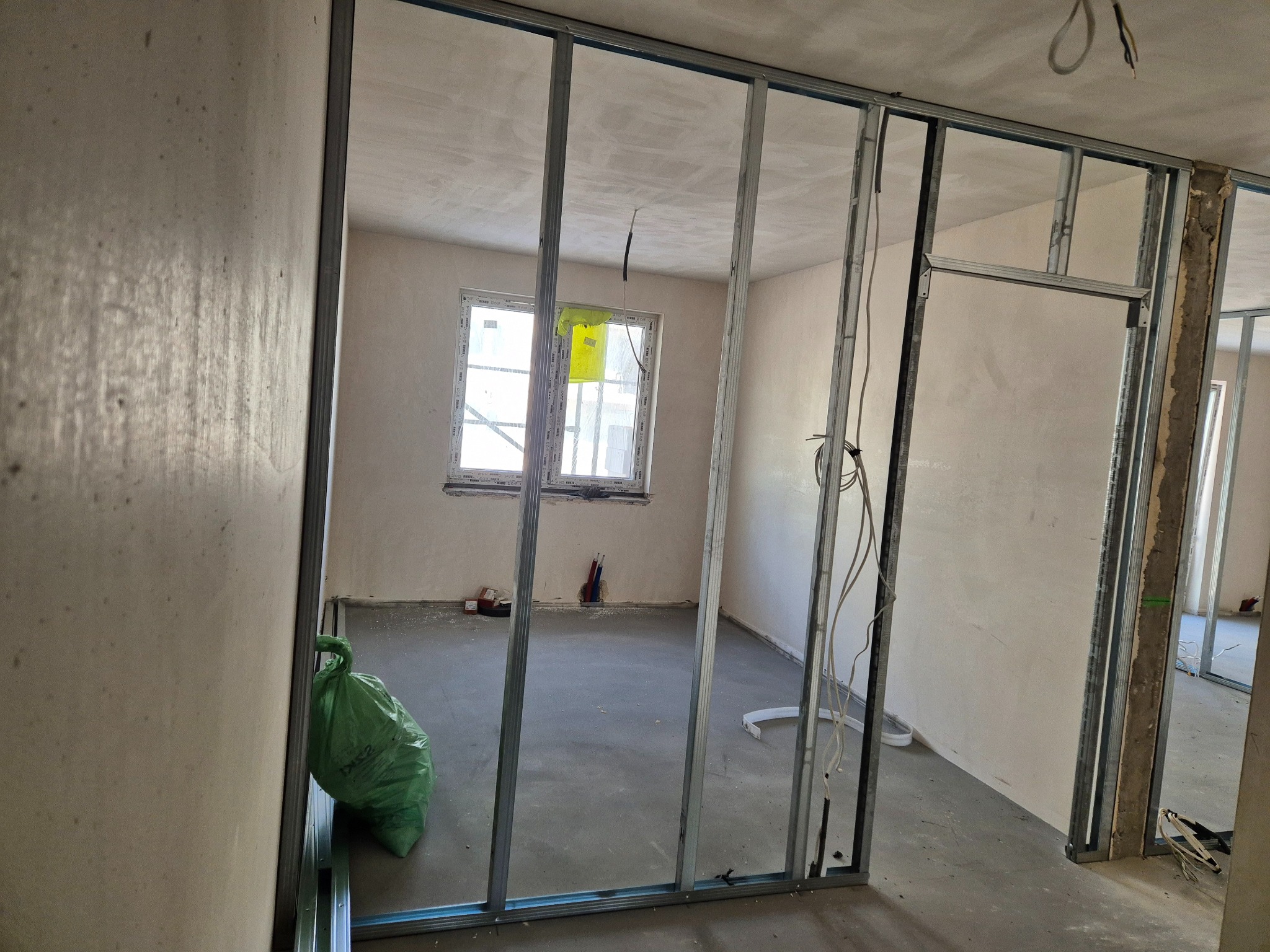 Wnętrze w trakcie tworzenia ścian działowych z metalowych profili. Widoczny szkielet konstrukcji, surowy beton na podłodze i worki z odpadami budowlanymi.