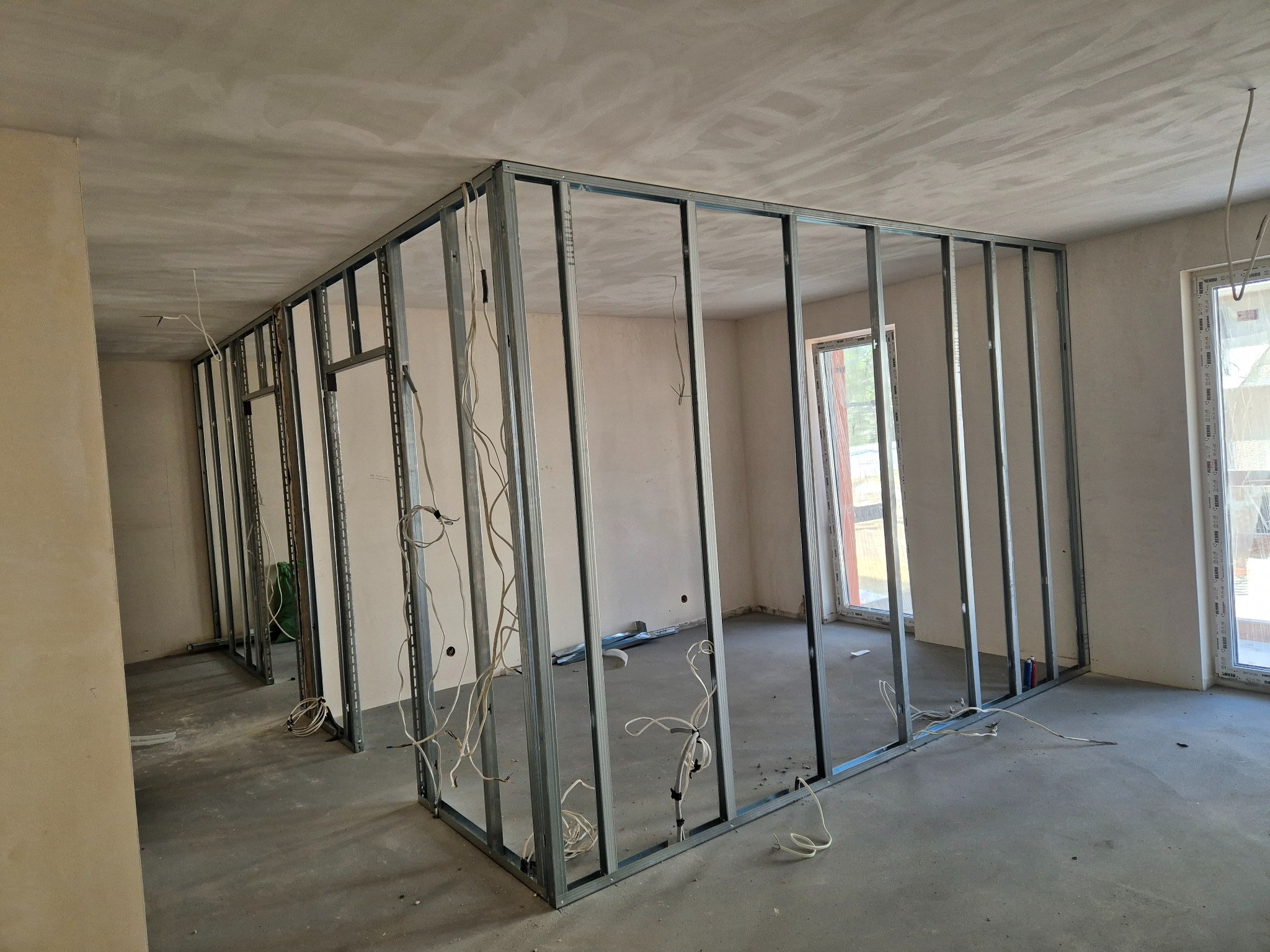 Metalowa konstrukcja ścian działowych w surowym wnętrzu. Widoczne profile, kable i okna. Etap prac wykończeniowych przed montażem.