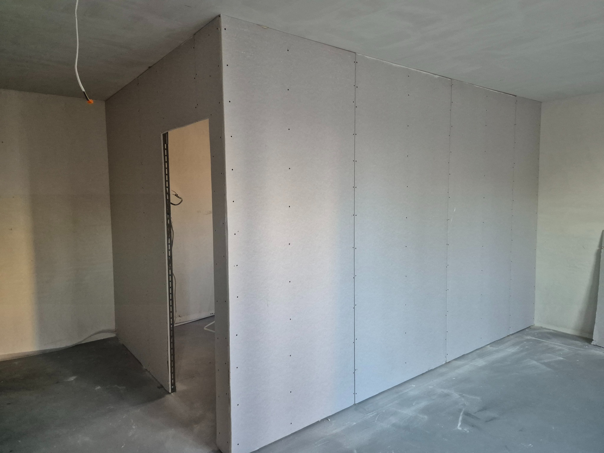 Ściana działowa z płyty KG z otworem drzwiowym w surowym wnętrzu. Realizacja z Lędzin. Widoczne łączenia płyt i surowy betonowy sufit.