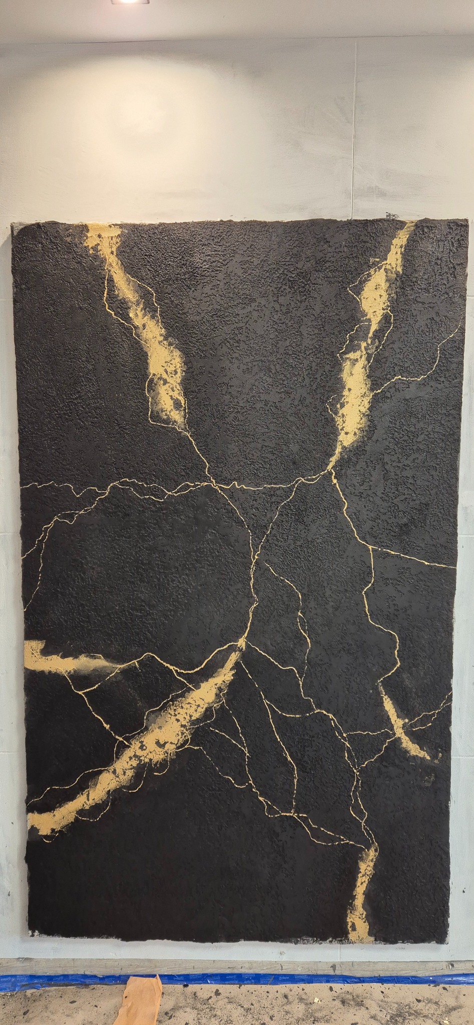 Czarna ściana z dekoracyjnym tynkiem imitującym żyły złota, wykończona w nowoczesnym stylu. Widoczne detale faktury i precyzja wykonania.