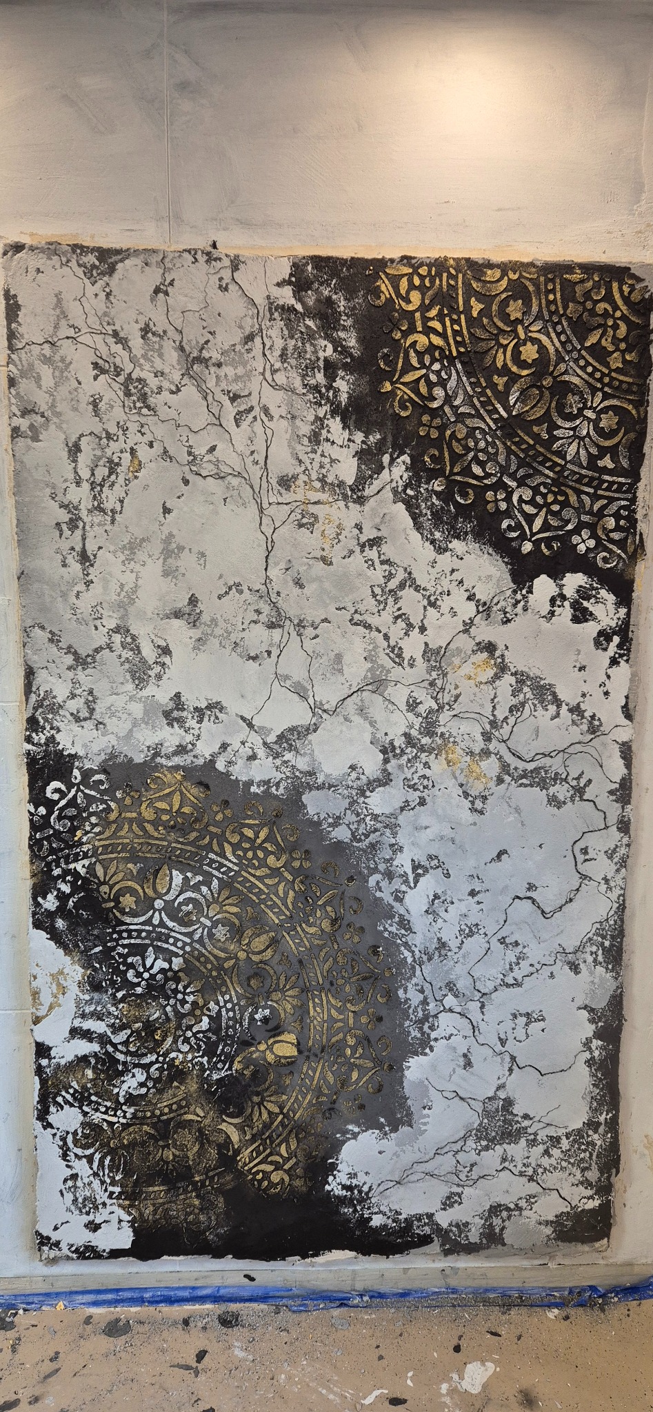 Dekoracyjny tynk na ścianie z ornamentami w kolorze złota, czerni i bieli. Widoczne detale wzoru i faktura tynku. Wykończenie wnętrza w stylu artystycznym.