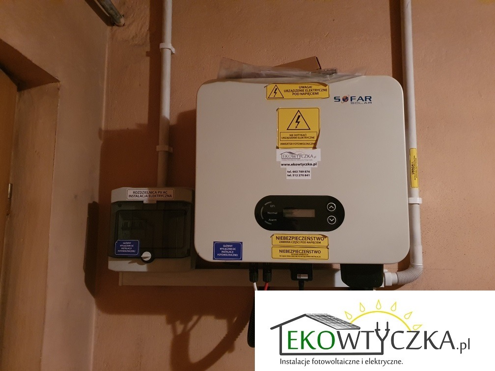 Biały inwerter Sofar Solar zamontowany na ścianie, obok rozdzielnica PV AC. Widoczne naklejki ostrzegawcze i logo firmy Ekowtyczka.pl.