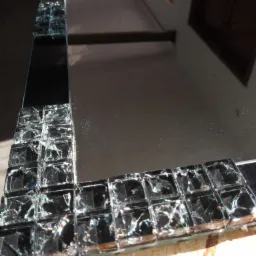 Szklane lustro z dekoracyjną ramą z mozaiki z potłuczonego szkła, widoczne refleksy światła na powierzchni.