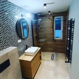 Nowoczesna łazienka z mozaiką na ścianie, drewnopodobnymi płytkami, kabiną prysznicową typu walk-in i umywalką nablatową na drewnianej szafce.