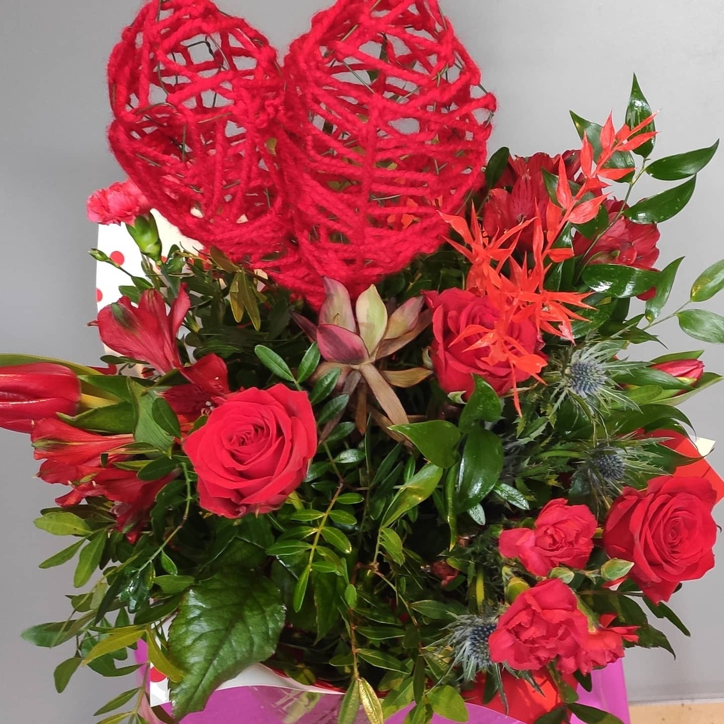 Czerwony bukiet z różami, alstromeriami i dekoracyjnymi sercami z czerwonej włóczki, umieszczony w pudełku w kropki.