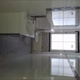 Nowoczesna łazienka z błyszczącymi, szarymi płytkami podłogowymi i ściennymi, białą szafką z umywalką i lustrem oraz oknem z białymi ramami, wykończona dekoracyjną listwą mozaikową.