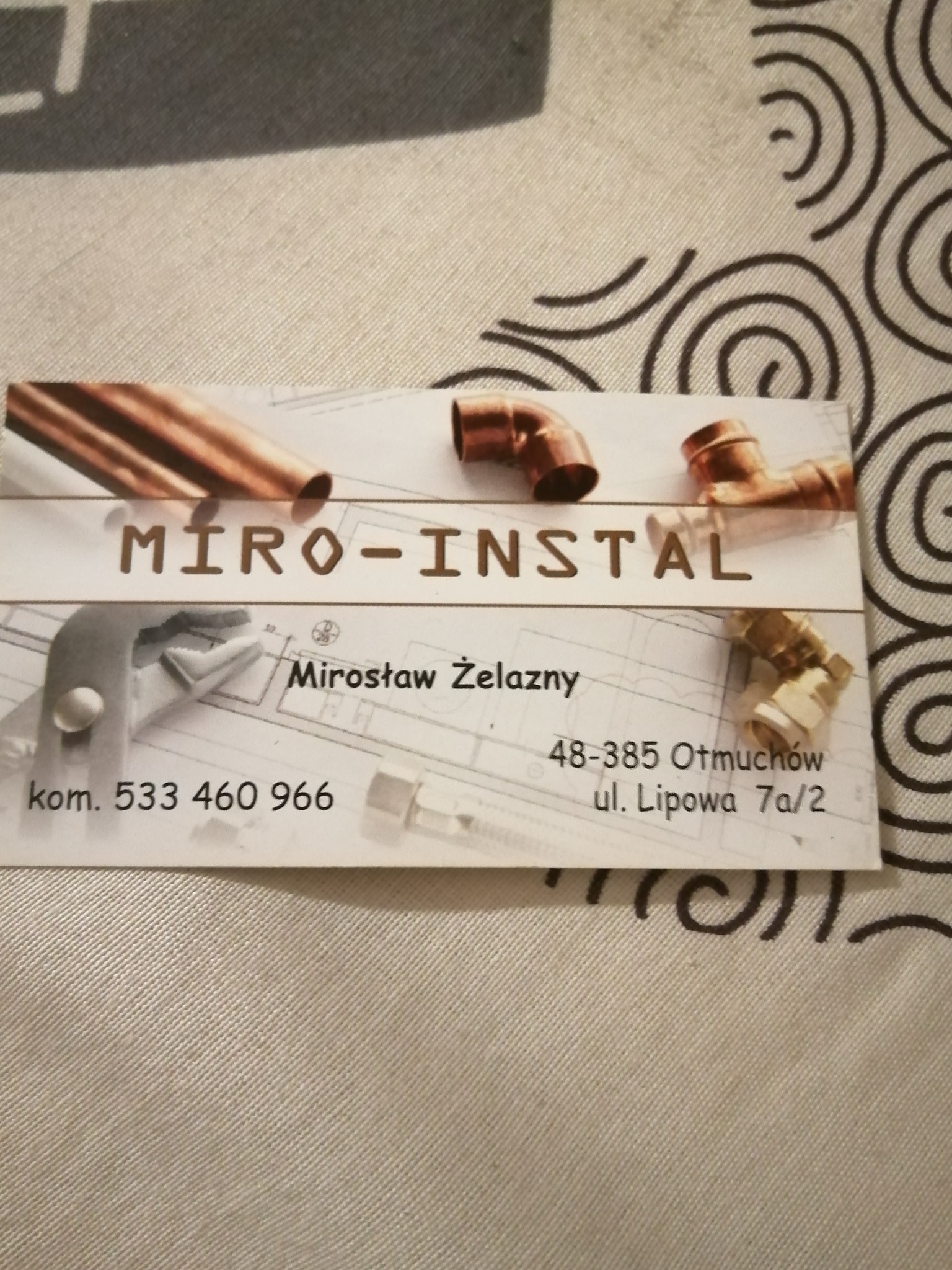 Wizytówka firmy Miro-Instal z grafiką przedstawiającą miedziane rury i złączki hydrauliczne na tle schematu instalacji.