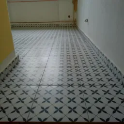 Nowa podłoga w łazience wyłożona biało-granatową płytką ceramiczną w kwiaty, widoczne niedokończone prace malarskie na ścianach i żółty fragment ściany.