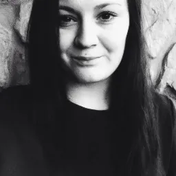 Portret uśmiechniętej kobiety na tle kamiennej ściany w czerni i bieli.