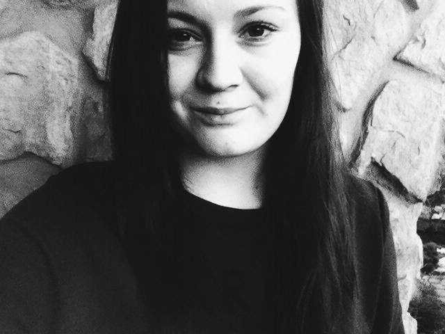 Portret uśmiechniętej kobiety na tle kamiennej ściany w czerni i bieli.