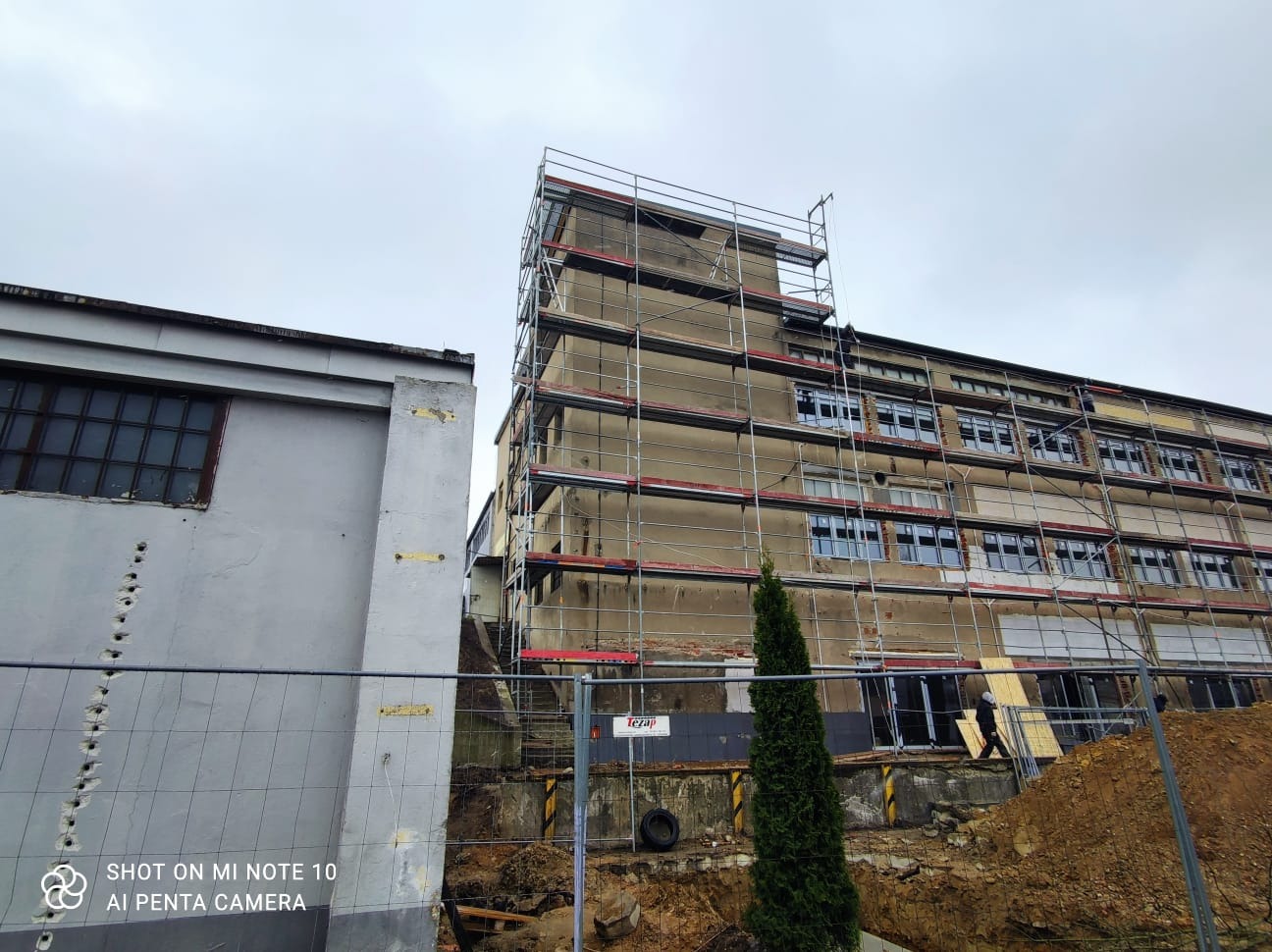 Remont elewacji wielopiętrowego budynku z użyciem rusztowań, widoczne fragmenty otynkowanej ściany i wykop ziemny.