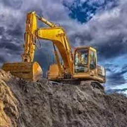 Żółta koparka na szczycie usypanej górki ziemi, tło burzowe chmury.