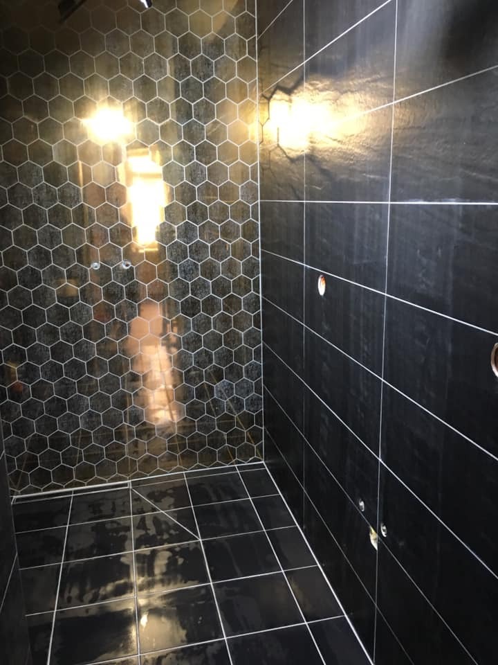 Kabina prysznicowa wyłożona czarnymi płytkami: heksagonalnymi na ścianie i kwadratowymi na podłodze, z jasnymi fugami i odbiciami światła.