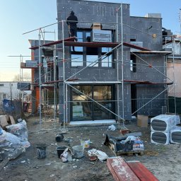 OSKOSTUDIO - Ocieplanie grafitowym styropianem budynku jednorodzinnego w Warszawie. Prace na rusztowaniu, widoczne puszki styropianu i narzędzia.