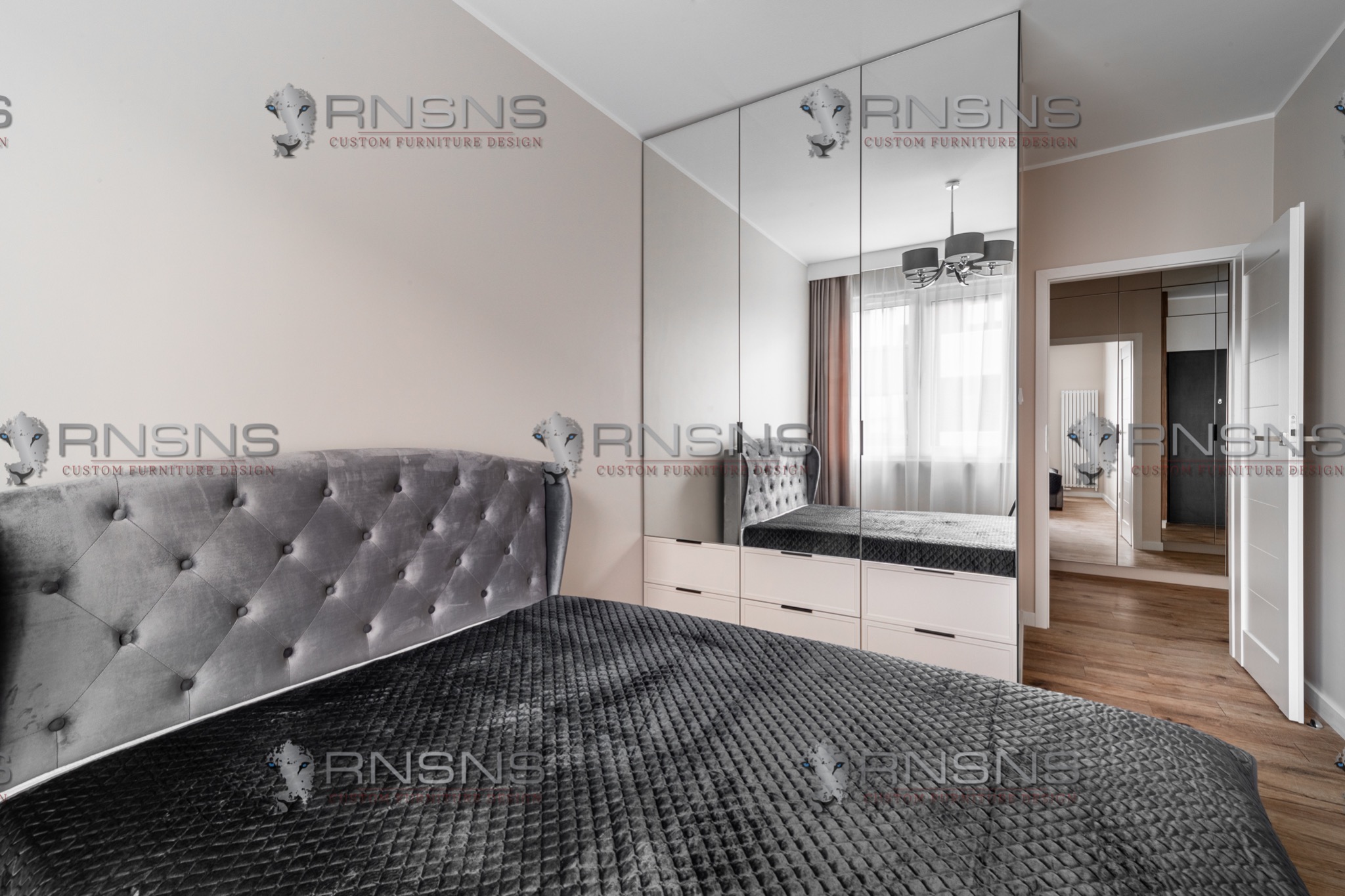 Sypialnia z dużym łóżkiem z szarym, pikowanym zagłówkiem i ciemną narzutą, szafa wnękowa z lustrzanymi drzwiami, widoczna w odbiciu część pokoju z oknem.