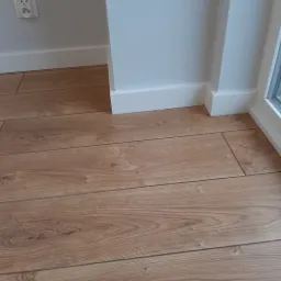 Ułożone panele podłogowe w Łodzi, widoczne listwy przypodłogowe i gniazdko elektryczne.