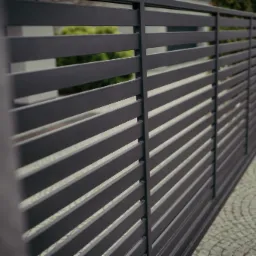 Nowoczesne, poziome przęsła ogrodzeniowe w kolorze grafitowym, widok z boku na tle kostki brukowej i zieleni.
