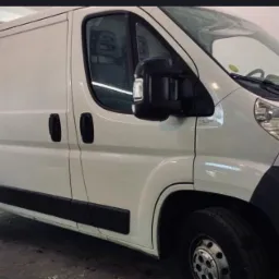 Biały bus dostawczy z otwartymi drzwiami kabiny, widok z boku na przednią część pojazdu, oświetlenie studyjne.