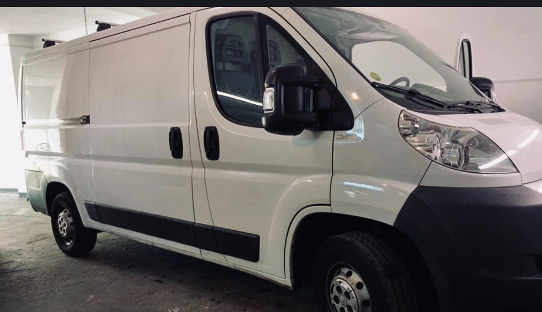 Biały bus dostawczy z otwartymi drzwiami kabiny, widok z boku na przednią część pojazdu, oświetlenie studyjne.