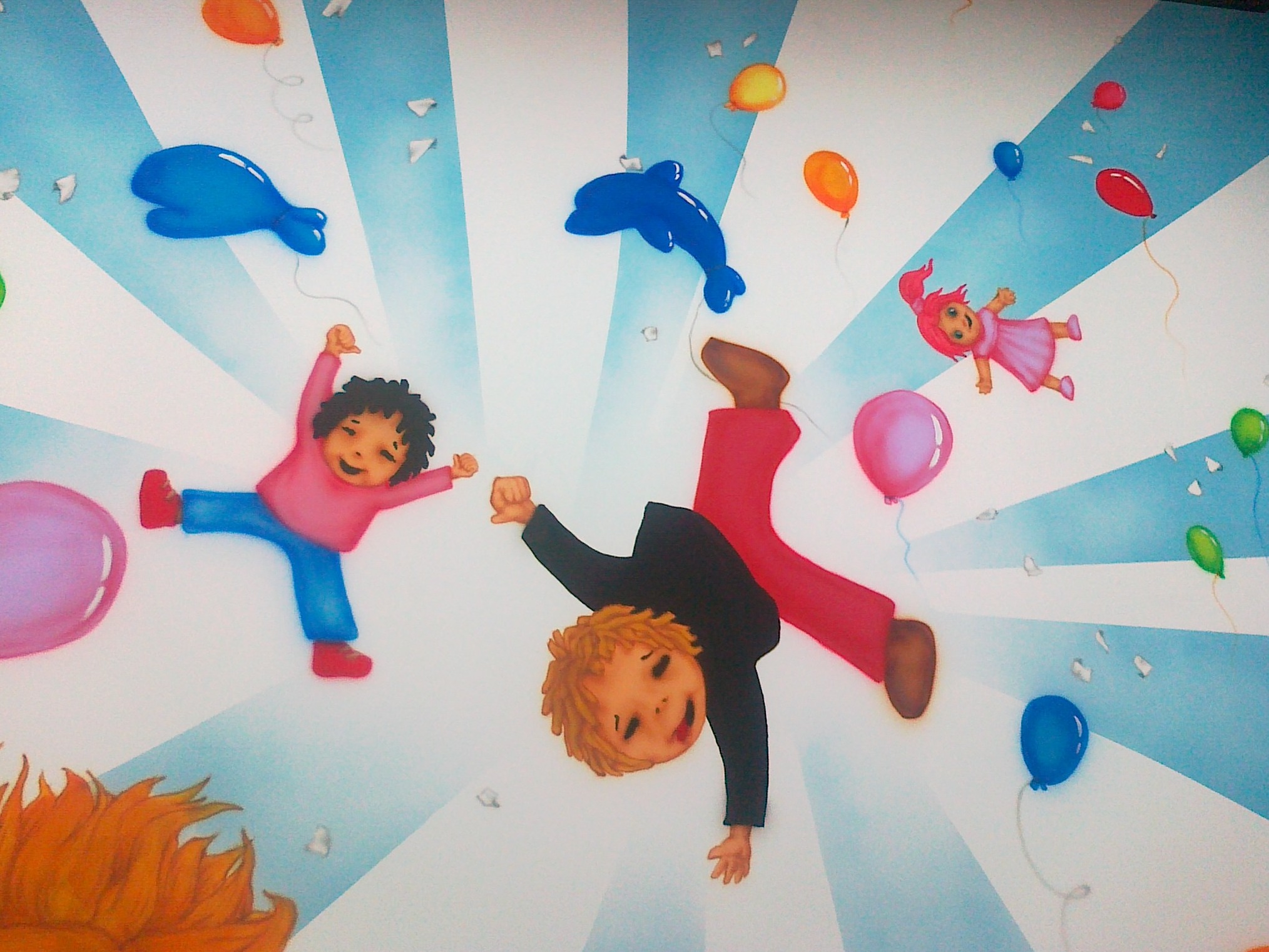 Ilustracja na ścianie przedstawiająca radosne postacie dzieci i zwierząt w otoczeniu balonów, utrzymana w jasnej, pastelowej kolorystyce z efektem promieniowania w tle.