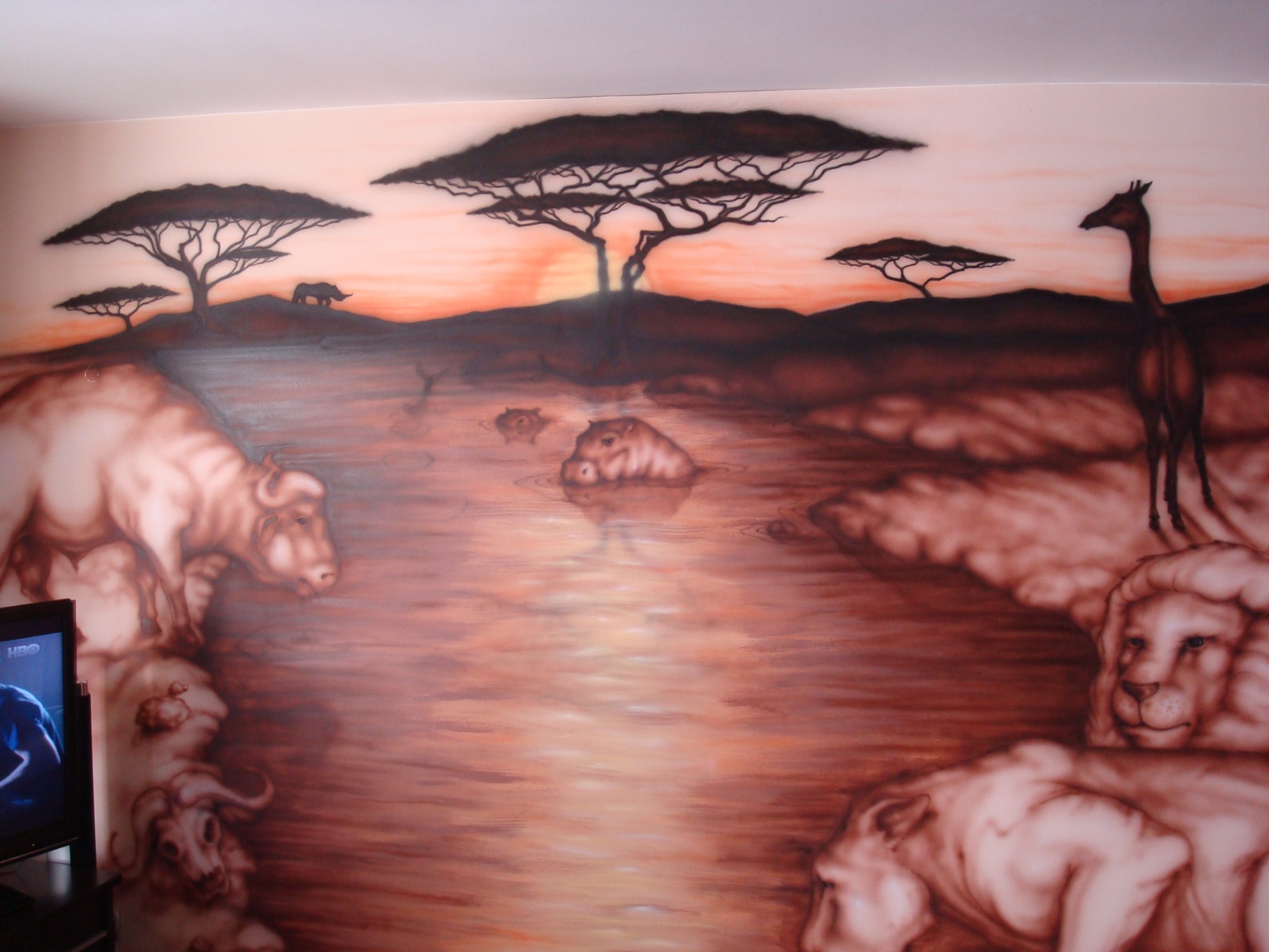 Afrykański krajobraz z sylwetkami zwierząt i drzew akacjowych, namalowany na ścianie, oświetlony zachodzącym słońcem, w odcieniach brązu i beżu.
