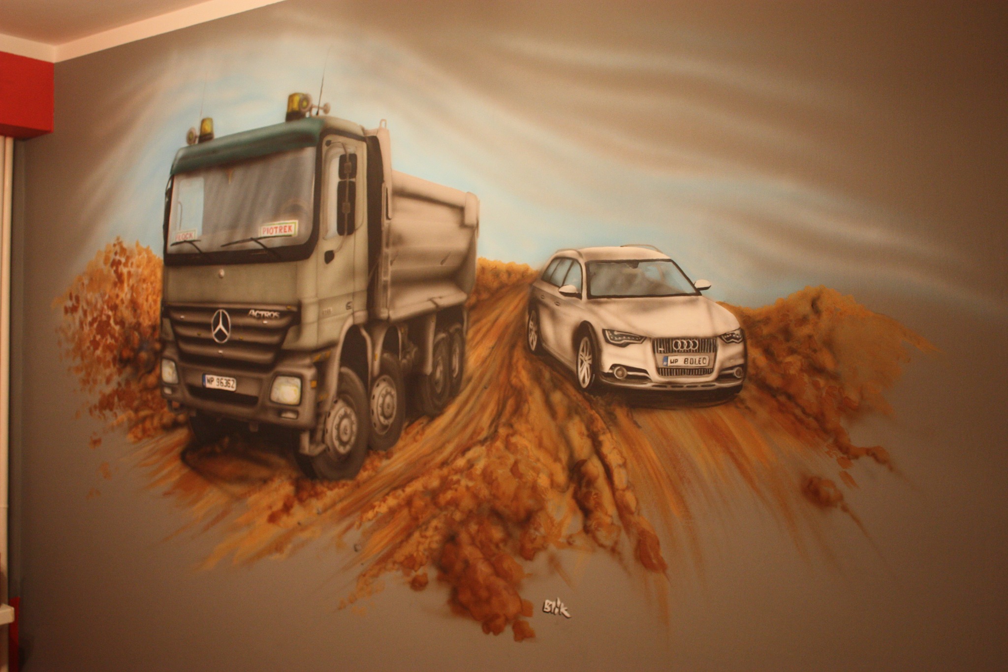 Ścienne malowidło przedstawiające ciężarówkę Mercedes Actros i samochód osobowy Audi A6 na tle piaszczystego krajobrazu, wykonane w technice aerografu z dbałością o detale.