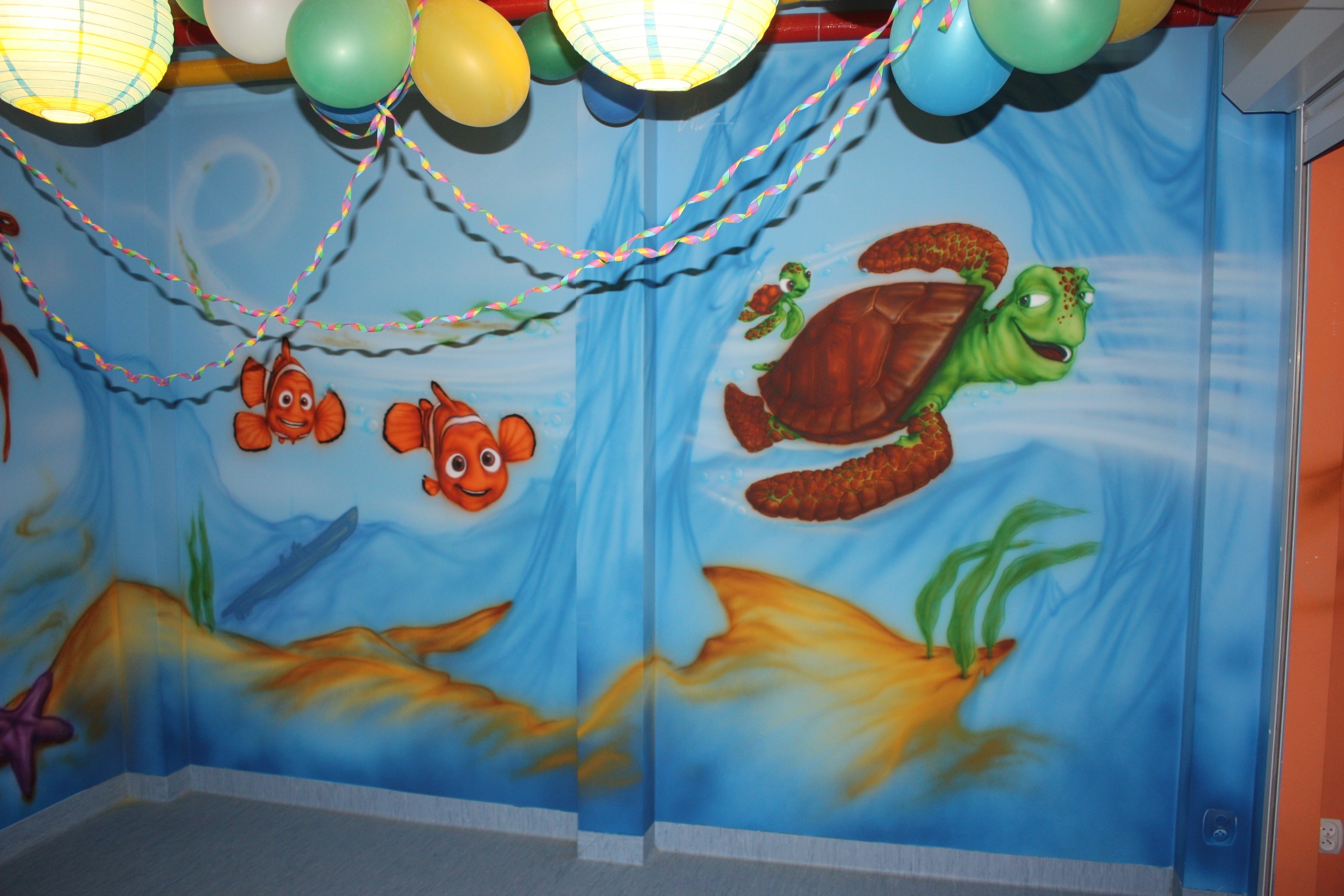 Pokój dziecięcy z muralem podwodnego świata z rybami Nemo i żółwiem, udekorowany balonami i serpentynami.