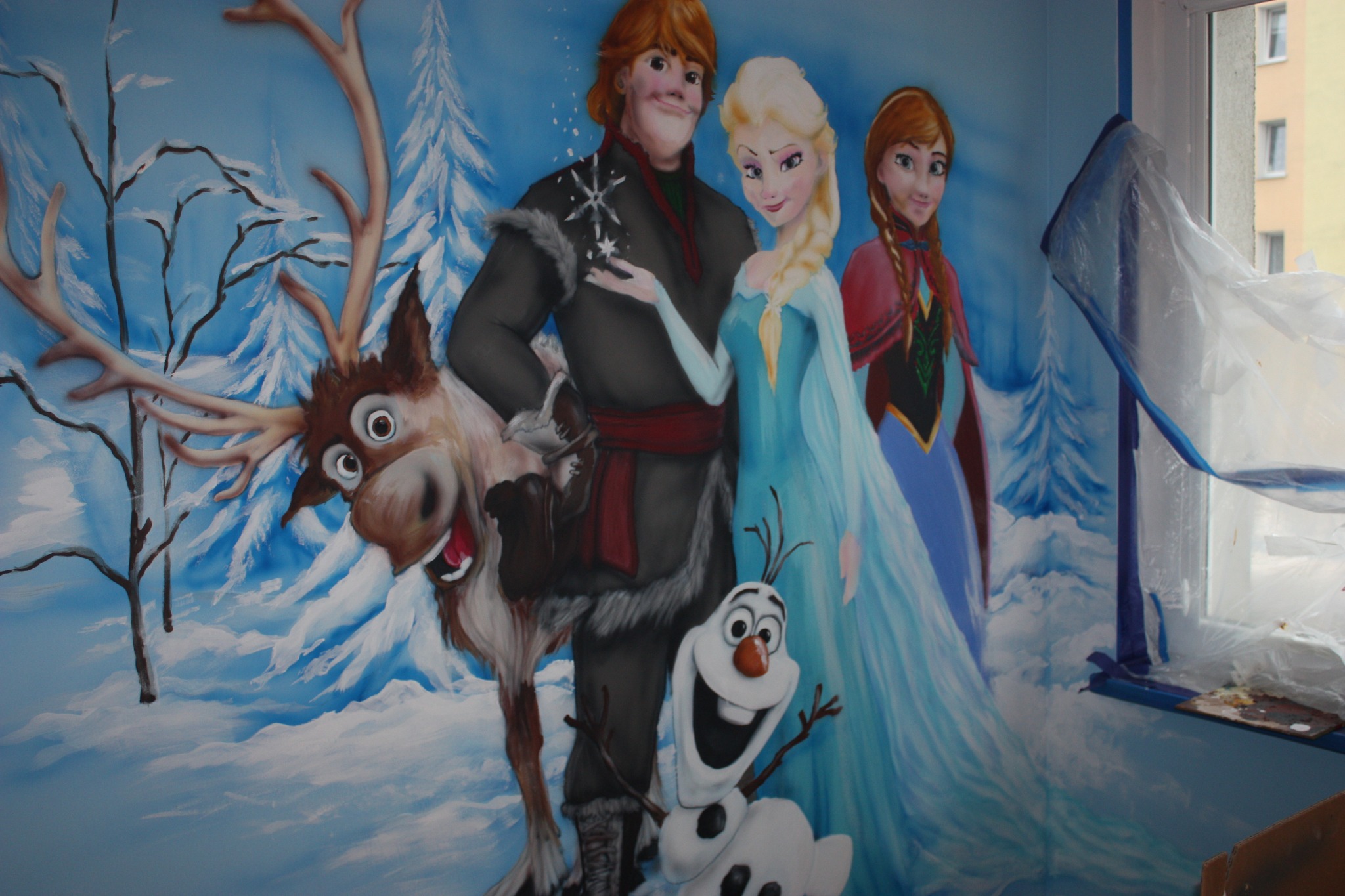 Ściana pokoju dziecięcego z ręcznie malowanym motywem z filmu 'Kraina Lodu', przedstawiająca Elzę, Annę, Kristoffa, Svena i Olafa, z widocznym zabezpieczeniem okna folią malarską.