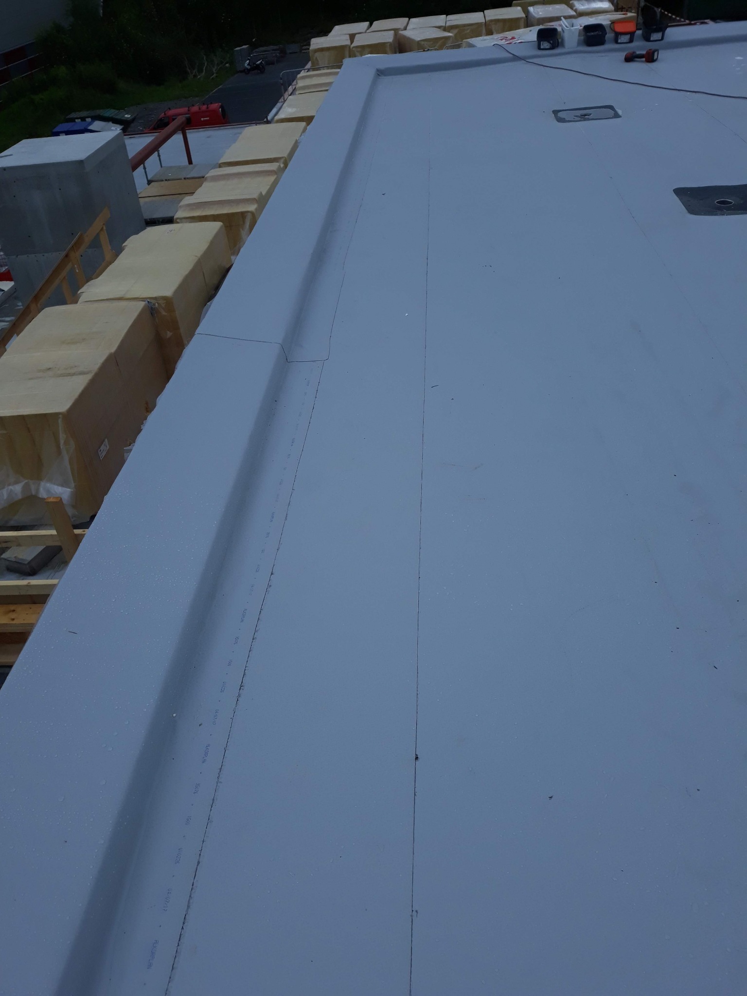 Szary, płaski dach pokryty membraną w Raszynie, widoczne łączenia i detale obróbek, w tle materiały budowlane przygotowane do dalszych prac.