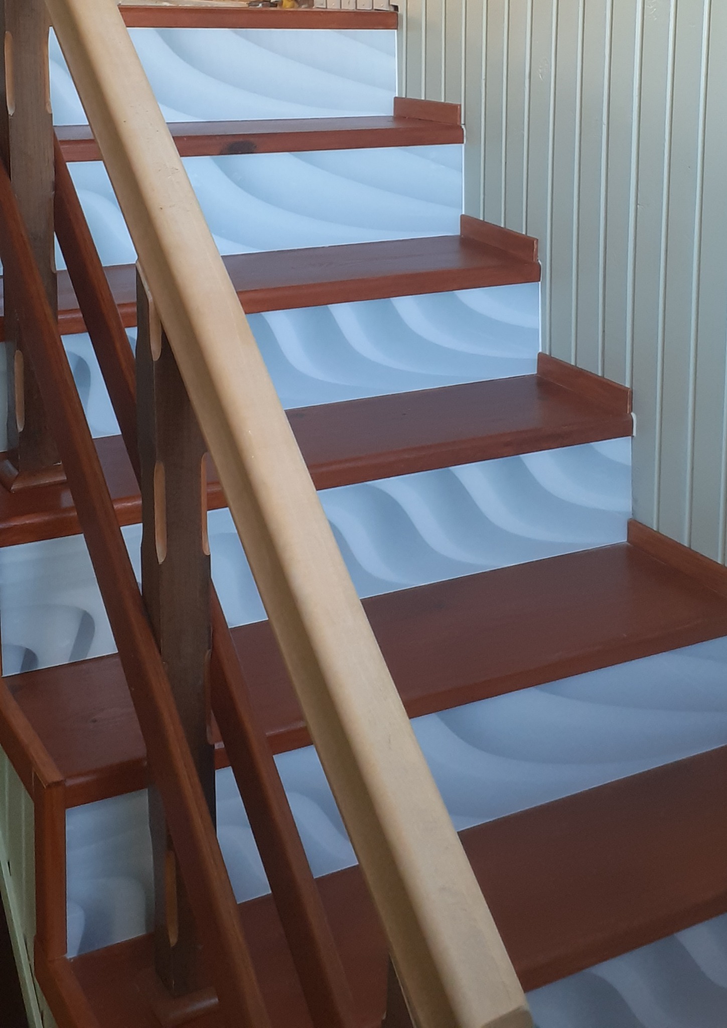 Drewniane schody z biało-niebieskim wzorem fal na stopniach, widok z dołu na poręcz.