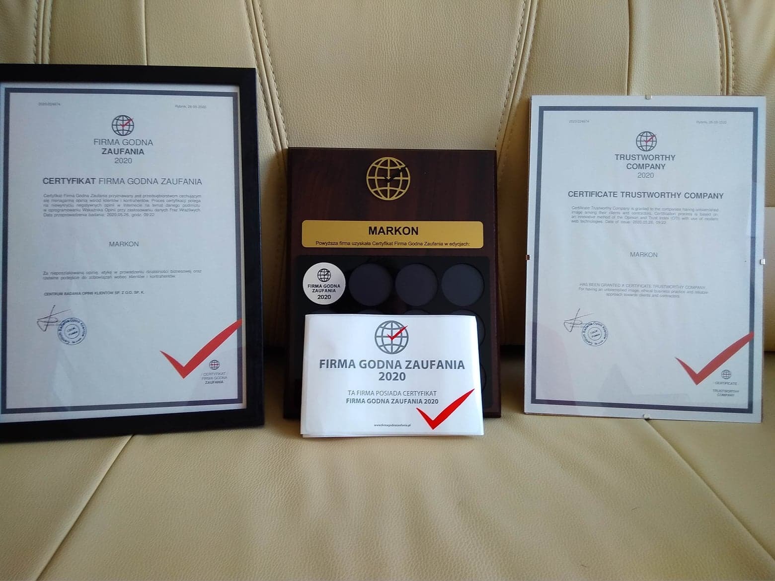 Prezentacja certyfikatów 'Firma Godna Zaufania' i 'Trustworthy Company' w ramkach i na drewnianej podstawce, z logo firmy MARKON.