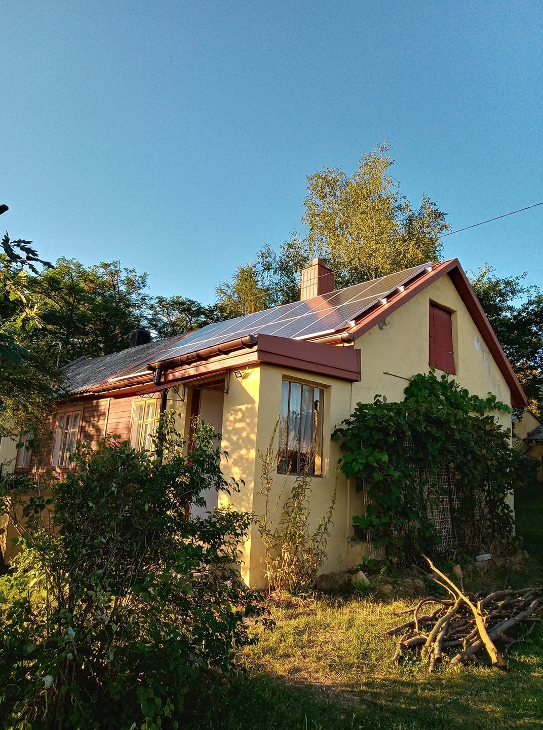 Dom jednorodzinny z panelami słonecznymi na dachu, widok z ogrodu w słoneczny dzień.