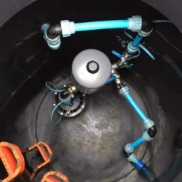 Wnętrze studni kręgowej z zamontowaną pompą głębinową, widoczne niebieskie rury instalacyjne i uchwyty do zejścia na dno studni.