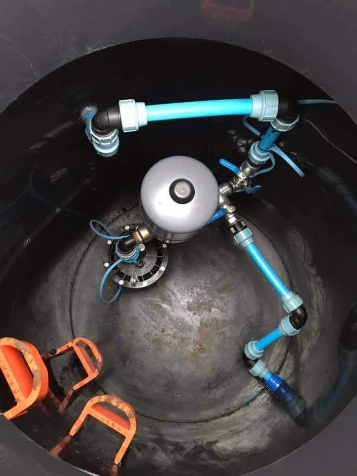 Wnętrze studni kręgowej z zamontowaną pompą głębinową, widoczne niebieskie rury instalacyjne i uchwyty do zejścia na dno studni.