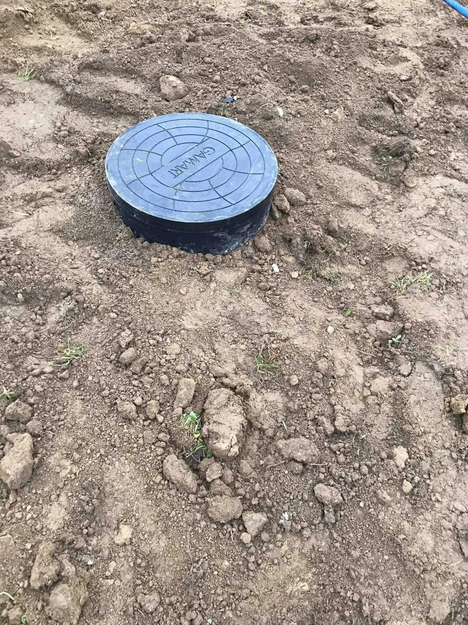 Czarne, okrągłe pokrycie studni z napisem 'GAMART' na ziemi.