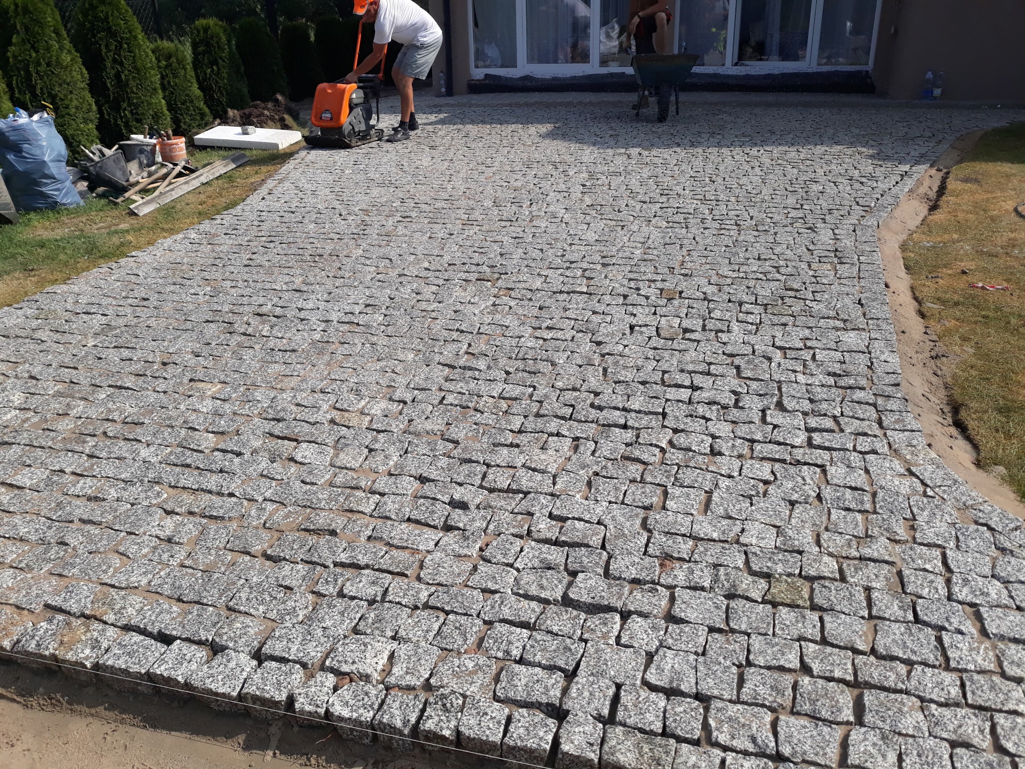 Ułożona nawierzchnia z kostki granitowej w Mińsku Mazowieckim, zagęszczana mechanicznie, widoczne narzędzia i materiały budowlane oraz pracownicy.