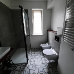 Nowoczesna łazienka z kabiną prysznicową typu walk-in, wiszącą toaletą i bidetem, wykończona płytkami podłogowymi w geometryczny wzór.