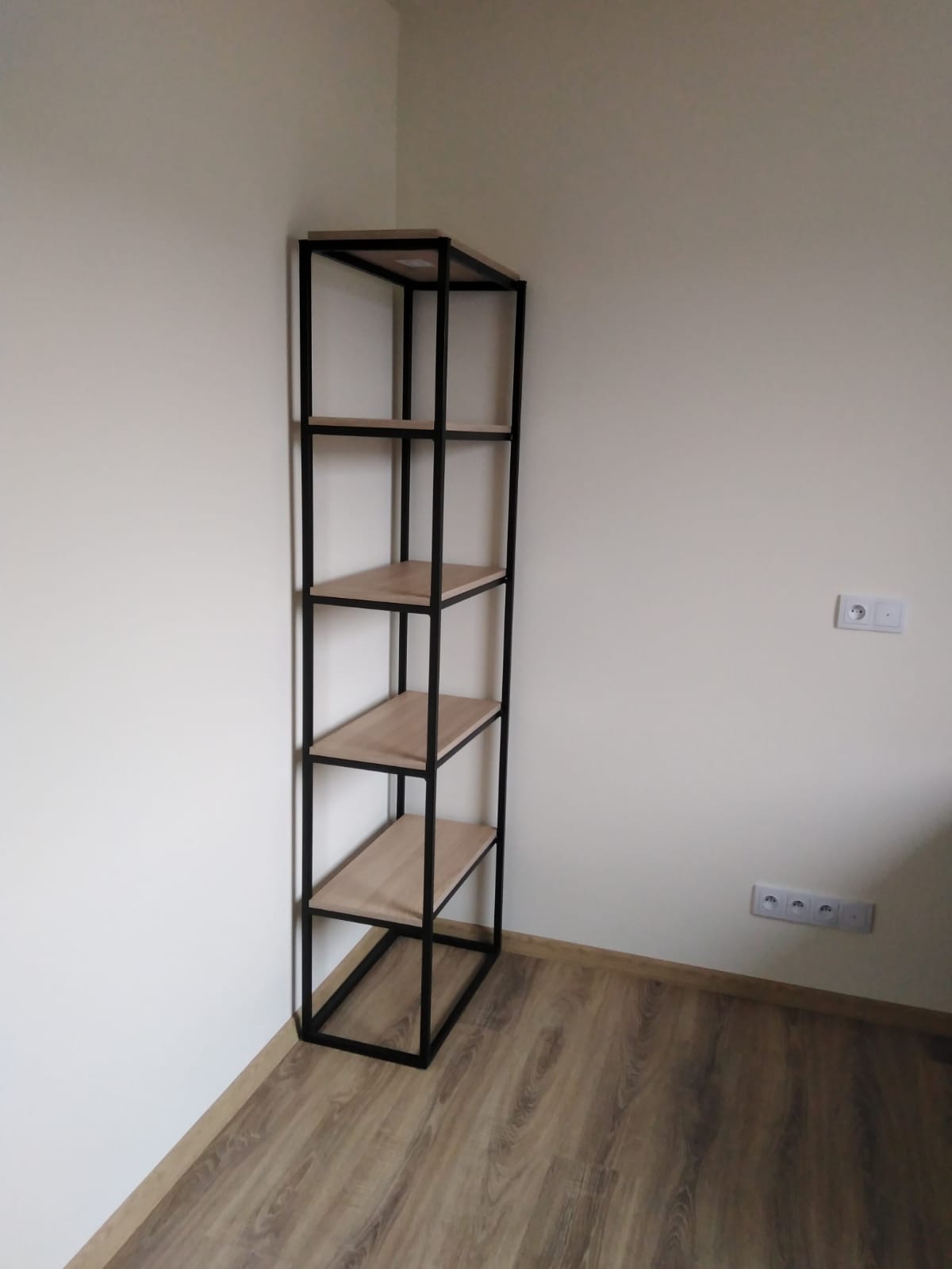 Metalowy regał z drewnianymi półkami, stojący w rogu pokoju z panelami podłogowymi.
