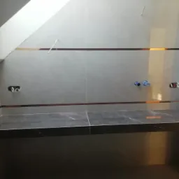 Ściana w łazience w trakcie wykańczania, szare płytki z dekoracyjnymi, poziomymi paskami, przygotowane otwory na armaturę, ciemny blat pod umywalkę.