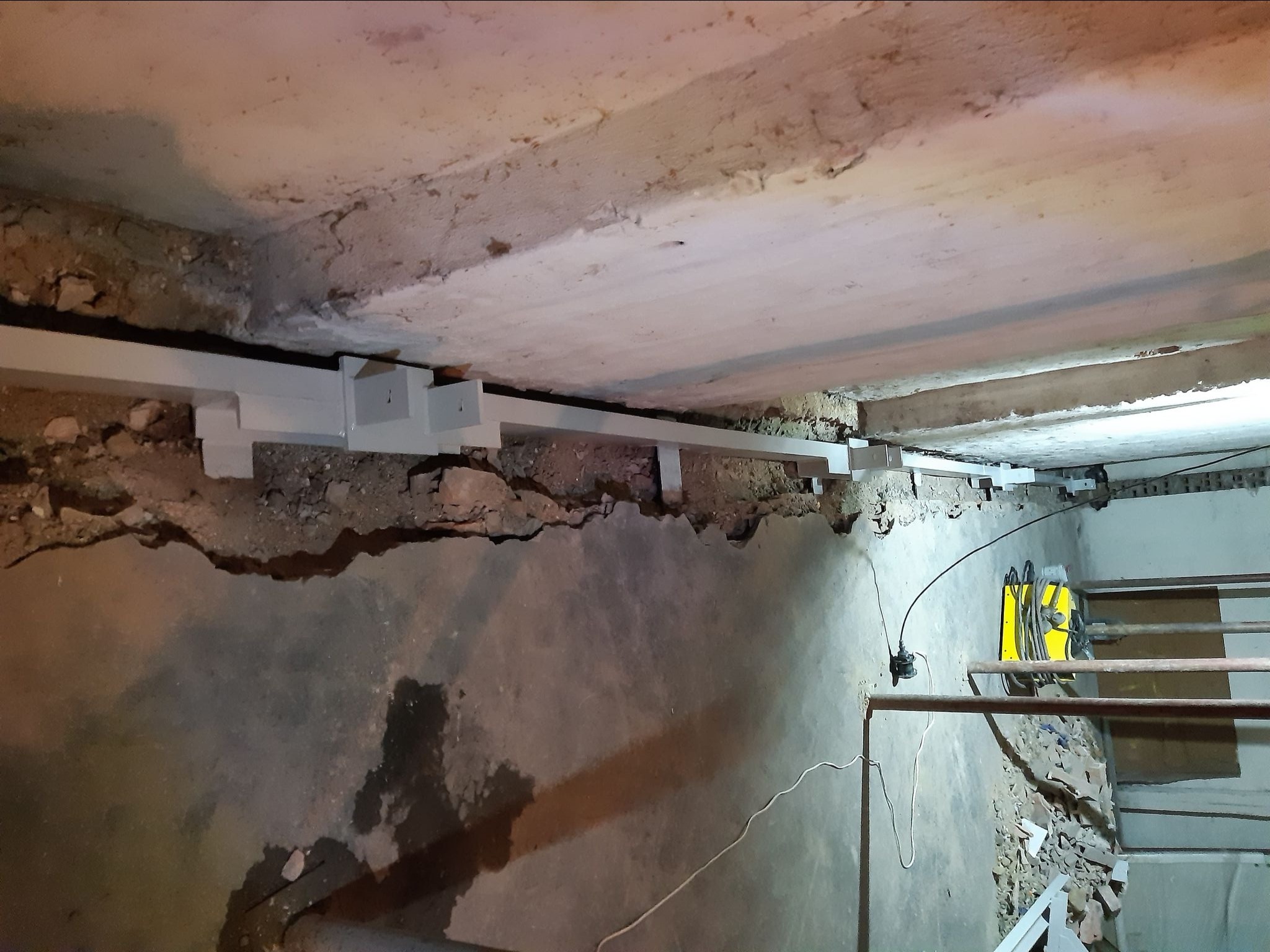 Wzmocnienie konstrukcji stropu w piwnicy za pomocą stalowych belek i wsporników, widoczny sprzęt spawalniczy.