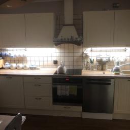 Marek Golebiewski - Jasna kuchnia w stylu rustykalnym z beżowymi płytkami, drewnianym blatem, białymi szafkami i okapem ozdobionym holenderskimi figurkami.