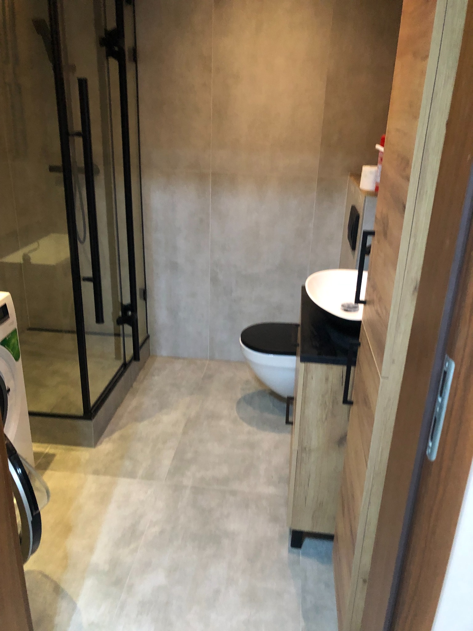 Nowoczesna łazienka po remoncie w Bydgoszczy: kabina prysznicowa z czarnymi ramami, umywalka nablatowa z czarną armaturą na szafce z drewnopodobnymi frontami, toaleta w stylu minimalistycznym...