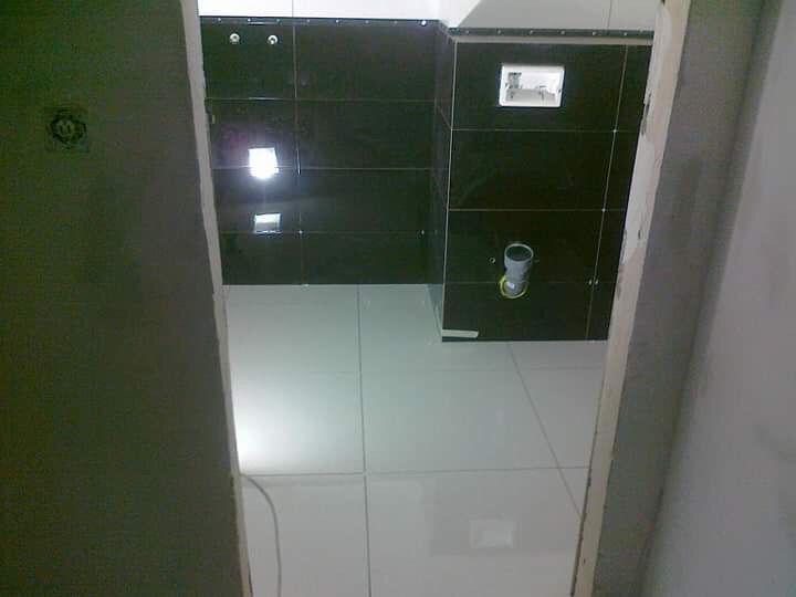 Wnętrze łazienki w trakcie remontu, widoczne czarne płytki na ścianie, białe płytki na podłodze, otwór na geberit oraz fragment futryny drzwi.